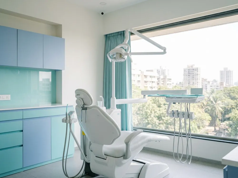 A clean, well-lit dental treatment room with a dental chair and soft blue cabinetry
